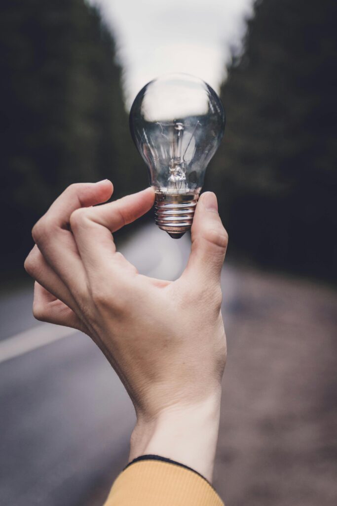 Close-up of a hand holding a lightbulb against a blurred outdoor road background.