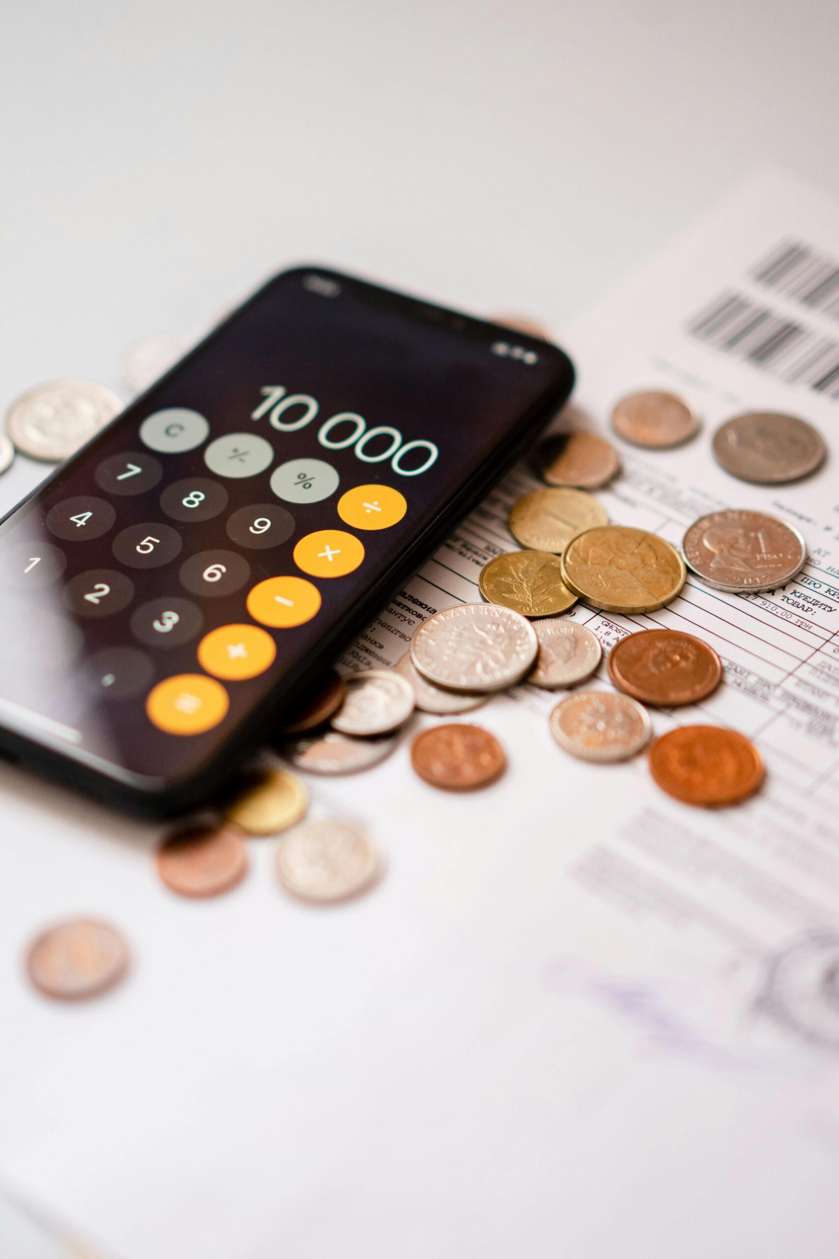 Smartphone calculator app displaying 10000 amidst scattered coins and documents.