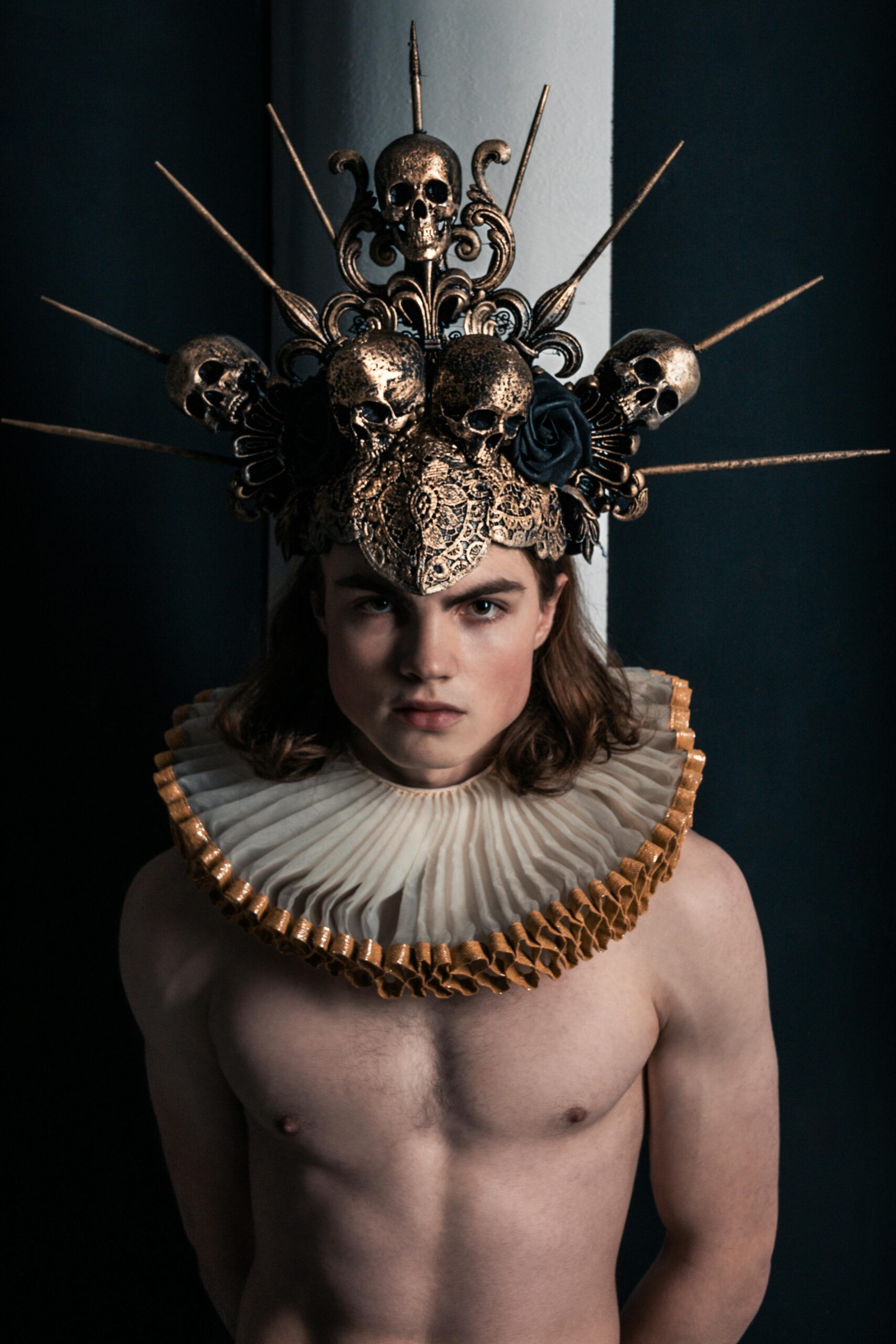Striking portrait of a shirtless man wearing a spiky crown and ornate collar, exuding dramatic flair in a studio setting.